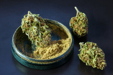herb grinder full of cannabis pollen surrounded by dry flowers of medical marijuana close up on black background 