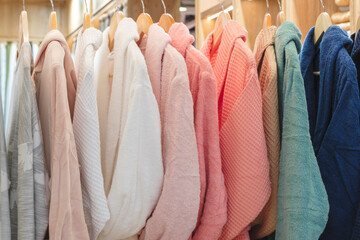 bathrobes of different colors hang on a hanger in the store - obrazy, fototapety, plakaty