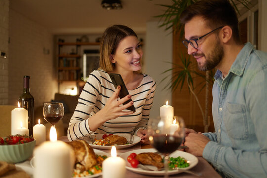 Happy couple enjoying food and wine while surfing the net on smart phone at home