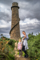 Mother and daughter standing in front of old and abandoned stone chimney with external spiral...