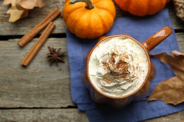 Fototapeta na wymiar Mug of pumpkin spice latte with whipped cream, ingredients and dry leaves on wooden table, flat lay. Space for text