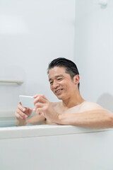 半身浴をしながらスマートフォンで動画を見る40代男性