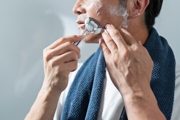 風呂上がりに洗面所で髭を剃る男性