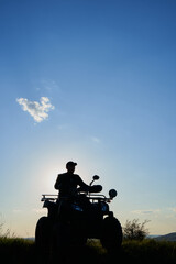 a man sits on a quad bike at sunset,shadow of a man on a quad bike, on a mountain in the evening © retbool
