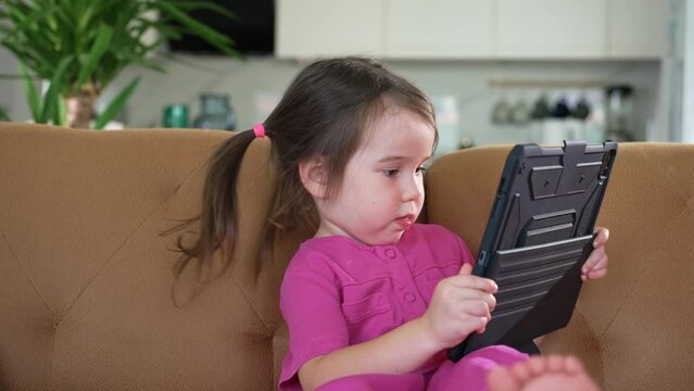 Little Girl Sitting on the Coach and Using a Digital Tablet