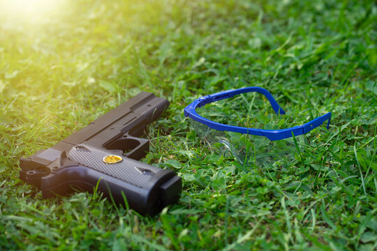A plastic pistol with airsoft goggles.Weapons for shooting training.A toy black pistol is lying on the grass.Games with weapons.