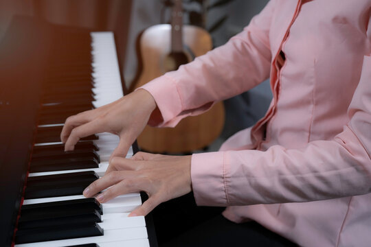 A woman in pink shirt press the key on paino with two hands, playing paino at home, relaxing time with music, music healing, increasing concentration with paino and improving brain concept.