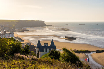 View over Arromanches beach and Cap Manvieux in Normandy, France, at sunset with remains of the WWII artificial Mulberry harbour lying on the sand and in the sea.