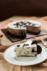 Oreo Cheesecake slice include chocolate, cream, sugar with fork and flowers served in plate isolated on napkin side view of cafe food