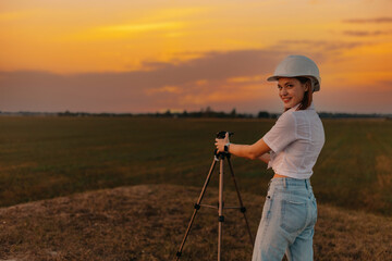 female engineer surveyor in a white helmet with a tripod in the field studying the location for the construction of a building - obrazy, fototapety, plakaty