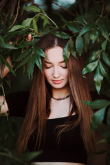 Fototapeta premium beautiful young woman posing in dark green foliage, girl face on summer nature, beauty and fashion concept