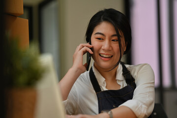 A Small business owner is talking on the phone and using a laptop to check online website orders confirming ecommerce shipping parcel delivery., running an e-commerce small business.