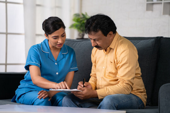 Indian Nurse Helping Recovered Patient To Fill Up Hospital Medical Documents At Home - Concept Of Insurance Policy, Guidance And Medical Assistance