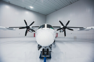 A twin-engine turbo prop aircraft parked in a hangar. The tow bar is attached to the front...