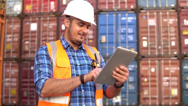 Container warehouse worker in uniform uses a digital tablet to inspect inventory in a large container yard. Logistics and export of business.