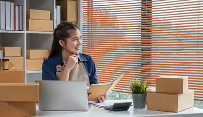 Attractive young Asian woman, startup business owner, working happily with boxes at home, preparing...
