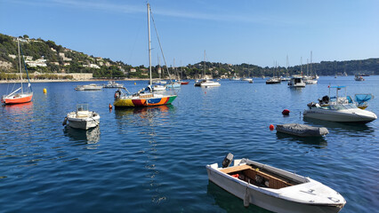 Villefranche-sur-Mer, France, October 2, 2021: View of Port Villefranche-Santé with boats, catamarans, sails boats, speed boats, and yachts moored to the pier, during daytime with a clear blue sky. - obrazy, fototapety, plakaty