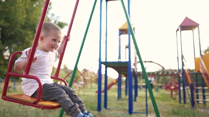 child rides on a swing in the park. happy family kid dream concept. child son swings on a swing at the playground. kid in kindergarten playing on swing outdoors lifestyle