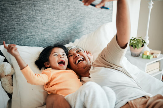 Selfie, grandmother and relax child on bed bonding, excited and love for happy family with care. Photography, technology and senior woman with little girl in bedroom on video call together in home.