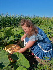 A young woman is trying to pick a large pumpkin from a garden bed.