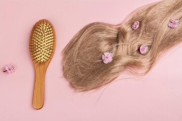 Long blond hair with sakura flowers and bamboo hair brush on pink background. International Hair Day. Bad Hair Day. Copy space
