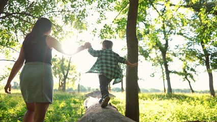 mom and baby boy play in the forest park. close-up child feet walk on a fallen tree log. happy family kid dream concept. mom and child in sneakers walk on a fallen tree in park lifestyle