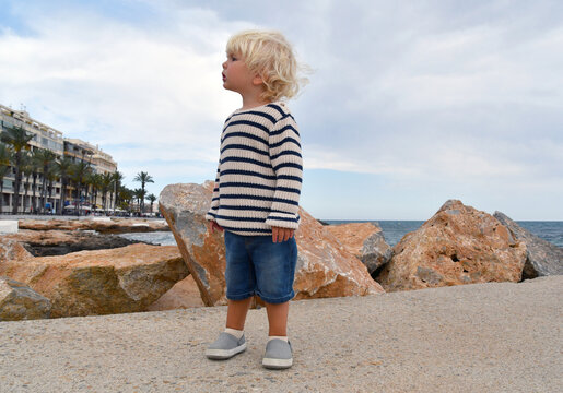 Cute little boy standing on the pier near the seaside promenade