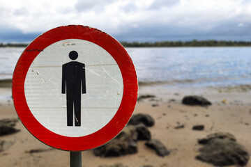 Dangerous area. pedestrians prohibited sign against backdrop of river bank. Pollution warning,...