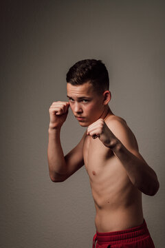 A teenage boxer athlete is training to box on dark background. Aggressive sport