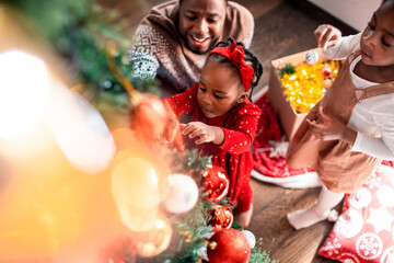 Young African American father decorating a Christmas tree with his children at their home