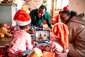 Young African American father surprises his children with a video call of their grandparents on a laptop at their home decorated for the Christmas and new year holidays