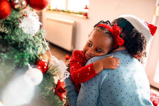 Young African American mother embracing her daughter in their home decorated for the Christmas and new year holidays