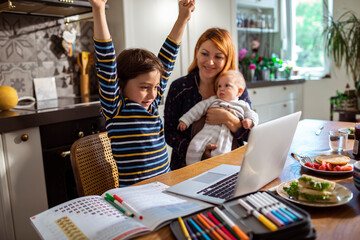 Young boy celebrating a passing grade on a laptop in the kitchen at home