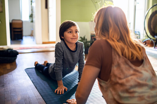 Young boy doing yoga with his mother in the living room at home