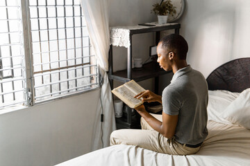 Man in gray shirt reading a book at home.