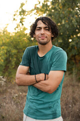 Portrait of an Arab guy enjoying the summer rain in the park, a young man in wet clothes looks at the camera smiling friendly