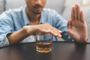 Alcoholism, depressed asian young man refuse, push out alcoholic beverage glass, drink whiskey, sitting alone at night. Treatment of alcohol addiction, having suffer abuse problem alcoholism concept. - obrazy, fototapety, plakaty