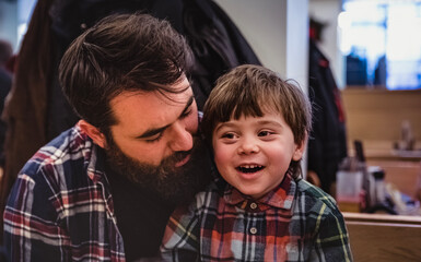 Happy and smiling nephew sitting on his uncle 's lap having fun moments indoor. Great time and big...