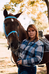 Obraz premium Woman holds a horse by the reins. Horseback riding in the autumn forest. Rental