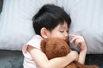 A boy is sleeping and hugging a teddy bear in bed.