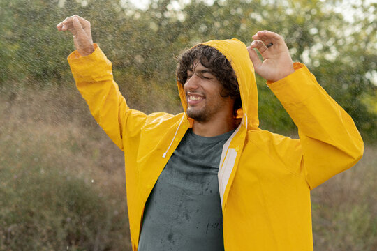 Joyful arabic guy enjoys his evening in the countryside by dancing in the rain. Playful young man spinning and enjoying a spring shower.