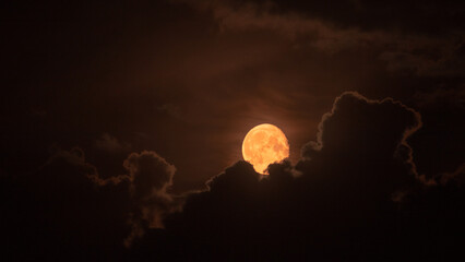 Orange moon behind the clouds close up