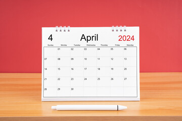 The April monthly desk calendar for 2024 year and pen on wooden table with red color background.