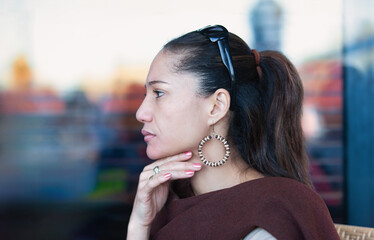 middle aged, multi ethnic beautiful woman sited at a coffeeshop, looking away in a pensive manner,...