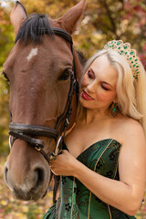 Fototapeta premium A woman in a long dress stands near a horse in an autumn forest. Riding
