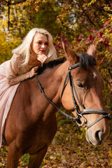 Fototapeta premium A woman in a long dress sits on a horse. Autumn forest, horse breeding