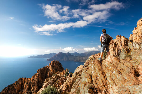 ein Wanderer steht in der Calanche einer bizarre Felsenlandschaft an der Suedkueste des Golfs von Porto im Regionalen Naturpark Korsika auf einem Felsen und schaut auf das Meer Korsika Frankreich