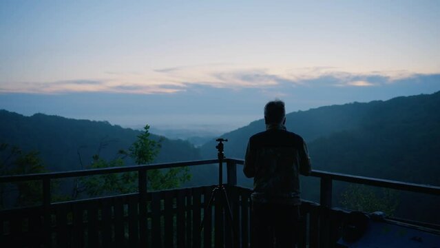 man operating analog camera at blue hour in nature with mountains and hills