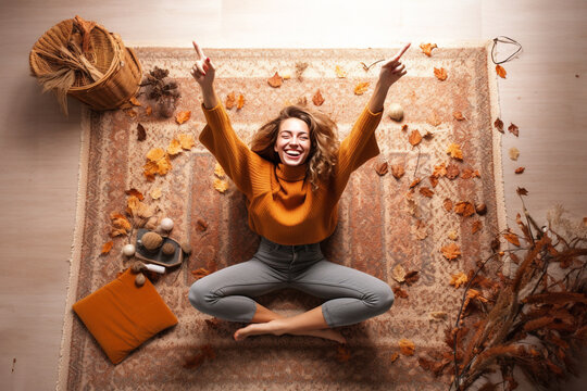 A picture of a young woman sitting on the carpet at home surrounded by autumn decorations making a victory sign with her fingers, happy thanksgiving photo
