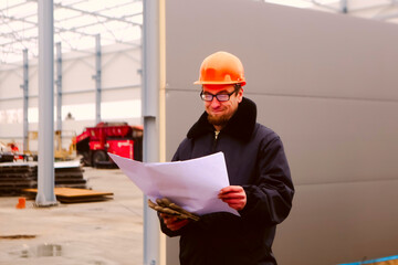 construction site engineer worker. portrait of smiling man in a hardhat and glasses at a construction site. Construction of a new building. Man looking at drawing